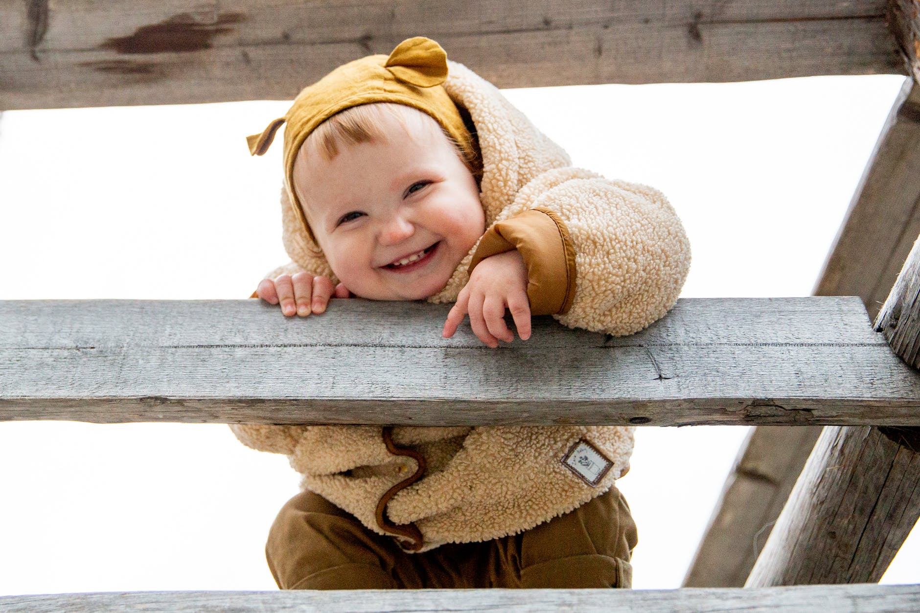 photo of baby leaning on wooden fence