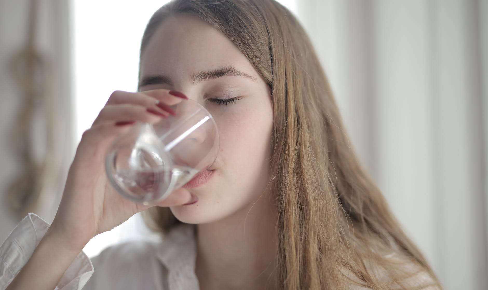 woman in white shirt drinking water from clear glass with her eyes closed