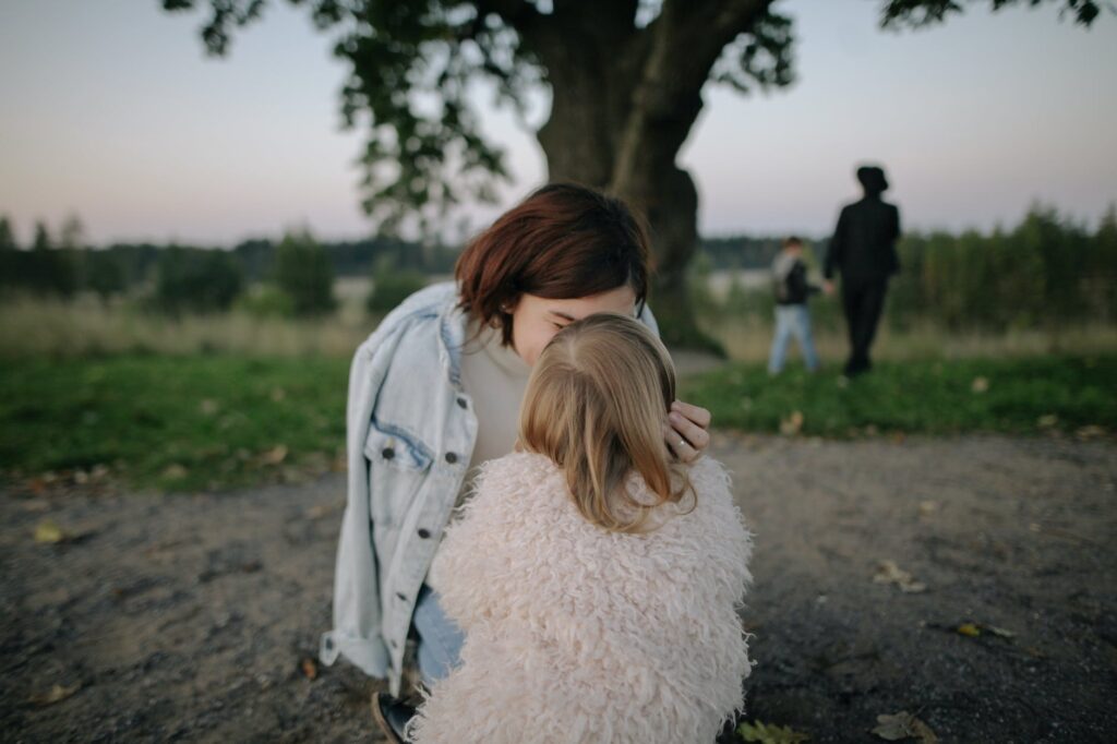 woman wearing light blue denim jacket kissing girl wearing white coat