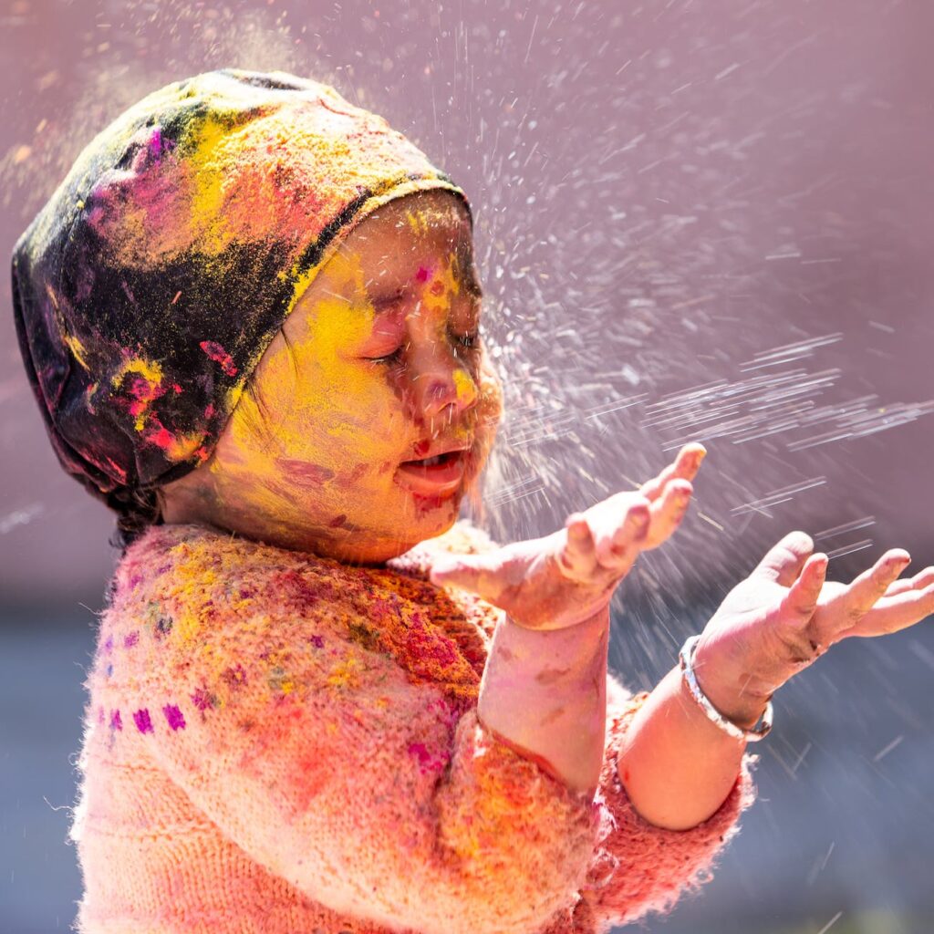 adorable ethnic girl playing with bright colors during holi festival