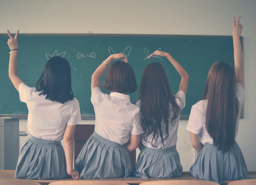 photo of four girls wearing school uniform doing hand signs