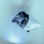 person in halloween makeup looking through a hole in fabric