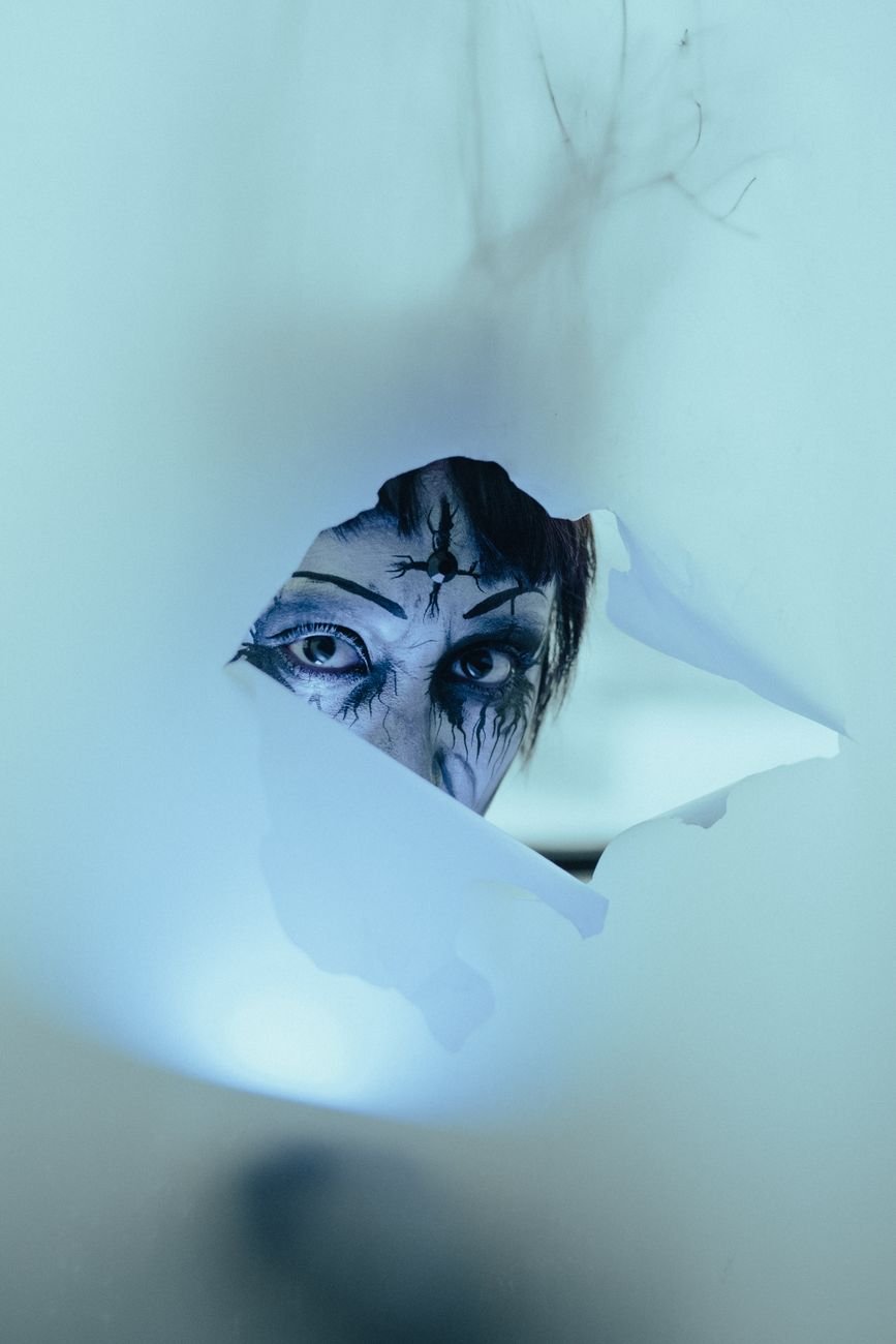 person in halloween makeup looking through a hole in fabric