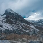 a mountain with snow and rocks under a cloudy sky